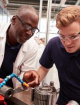 Two men in safety goggles work on lab equipment